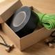 Kraft paper gift box containing a roll of black gaff tape, coiled bright green 550 paracord, and bamboo Bongo Ties with elastic loops on a wooden surface